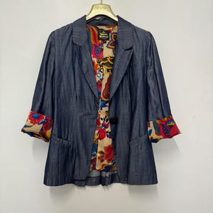 May include: A dark blue blazer with a single button closure and three-quarter length sleeves. The interior lining and sleeve cuffs feature a vibrant, multi-colored floral and paisley pattern. A Vivienne Westwood London label is visible inside.