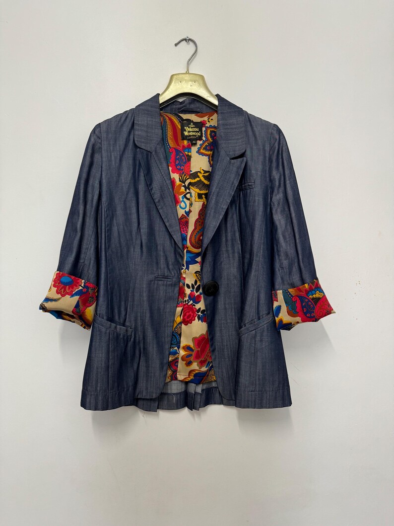May include: A dark blue blazer with a single button closure and three-quarter length sleeves. The interior lining and sleeve cuffs feature a vibrant, multi-colored floral and paisley pattern. A Vivienne Westwood London label is visible inside.