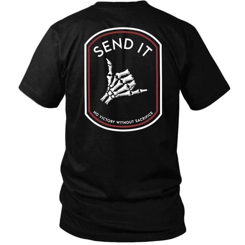 May include: Black t-shirt featuring a white and red emblem with the words "SEND IT" above a skeleton hand making a shaka sign. The emblem also includes the text "NO VICTORY WITHOUT SACRIFICE".