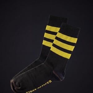 May include: A pair of black socks with three horizontal yellow stripes near the top. The text "FIRST OFFICER" is printed in yellow on the side of the socks.
