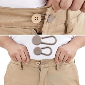 May include: A tan pair of trousers featuring an adjustable waistband extender. The device consists of a circular button attached to a flexible, looped strap that secures around the existing button of the pants to provide extra waist room.