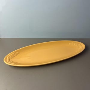 May include: A long, oval-shaped serving platter in a bright yellow color. The platter has a slightly raised rim with a decorative design at each end. The surface is smooth and glossy, suitable for serving food.