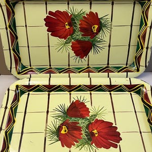 May include: Two vintage metal serving trays. The trays have a pale yellow background with a grid pattern and a floral design featuring red flowers with yellow centers and green leaves. The edges are decorated with a geometric pattern in green, brown, and yellow.