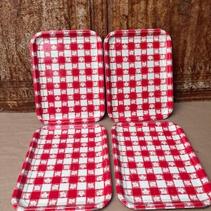 May include: A set of four rectangular metal trays featuring a red and white checkered pattern with small white maple leaf icons printed within the red squares. Each tray has rounded corners and slightly raised edges for a functional design.