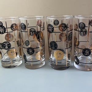 May include: Set of four vintage highball glasses. Each clear glass is decorated with gold and black coin designs, connected by black lines. The glasses have a classic, cylindrical shape, perfect for serving cocktails or other beverages.