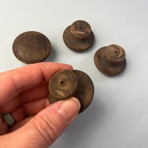 May include: Four round, dark brown wooden knobs with a smooth, matte finish. Each knob features a flat, circular top surface and a smaller, cylindrical base with a centered hole, showing a consistent, weathered, and natural wood grain texture.