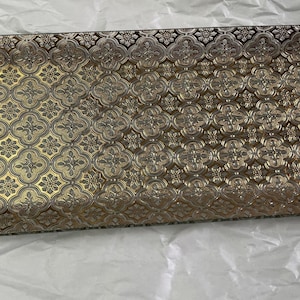May include: Rectangular decorative tray with a gold and bronze floral pattern. The tray has a raised edge and a detailed, embossed design. The color palette includes gold, bronze, and dark brown, creating a luxurious aesthetic. Ideal for serving or display.