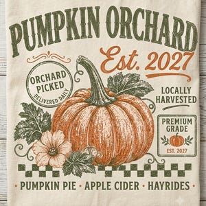 Può includere: Una t-shirt color crema con la grafica di una grande zucca arancione con foglie verdi e un fiore. Il testo recita PUMPKIN ORCHARD, Est. 2027, ORCHARD PICKED DELIVERED DAILY, LOCALLY HARVESTED, PREMIUM GRADE e PUMPKIN PIE APPLE CIDER HAYRIDES.