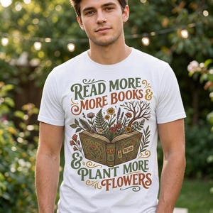 Può includere: Una t-shirt bianca con la grafica di un libro aperto da cui crescono vari fiori e piante. Il testo recita "READ MORE BOOKS & PLANT MORE FLOWERS", con la scritta "READ" sul dorso del libro e su un'etichetta attaccata.