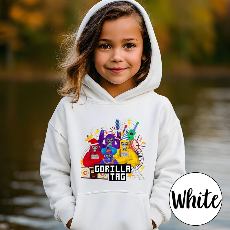 Puede incluir: Una sudadera con capucha blanca con un gr&aacute;fico colorido de monos de dibujos animados tocando instrumentos musicales. El texto "GORILLA TAG" se muestra debajo. La sudadera con capucha la lleva una persona joven.