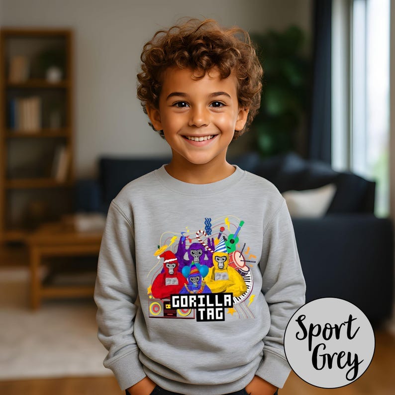 Puede incluir: Sudadera gris deportiva con un gr&aacute;fico colorido de gorilas de dibujos animados tocando instrumentos musicales. El texto "GORILLA TAG" est&aacute; impreso debajo. La sudadera la lleva un ni&ntilde;o.