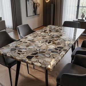 May include: A rectangular dining table featuring a polished surface composed of numerous inlaid agate slices in shades of brown, grey, and cream, supported by four slender black metal legs, surrounded by six dark grey upholstered armchairs.