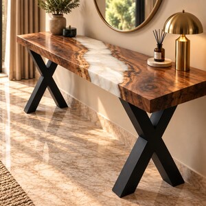 May include: A long console table featuring a natural wood slab top with a central white resin river inlay. The table is supported by two black metal X-shaped legs. The wood grain is visible, and the surface is smooth with a polished finish.