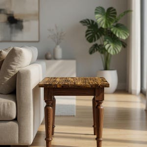 Puede incluir: Una pequeña mesa auxiliar de madera con una tapa de estilo mosaico y cuatro patas torneadas. La mesa es de color marrón cálido y está colocada junto a un sofá beige. Sus dimensiones son de aproximadamente 61 cm de altura y 46 cm de ancho.