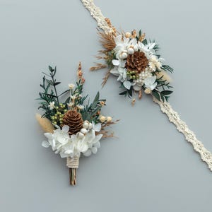 Peut inclure: Un ensemble de boutonni&egrave;re et de corsage de poignet avec des fleurs s&eacute;ch&eacute;es, des pommes de pin et de la verdure. La boutonni&egrave;re est envelopp&eacute;e de ficelle. Le corsage de poignet est fix&eacute; &agrave; un bracelet en dentelle cr&egrave;me.