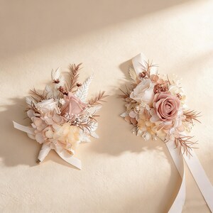 K&ouml;nnte beinhalten: Zwei Blumenarrangements mit Rosen und anderen Bl&uuml;ten in Rosa, Creme und Beige. Die Str&auml;u&szlig;e sind mit cremefarbenen B&auml;ndern gebunden. Einer ist ein Anstecker, der andere ein Handgelenks-Corsage.