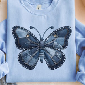 Può includere: Felpa azzurra con un design a farfalla in denim. La farfalla è realizzata con toppe di denim blu di diverse tonalità, cucite con filo bianco. La felpa ha un girocollo e maniche lunghe.