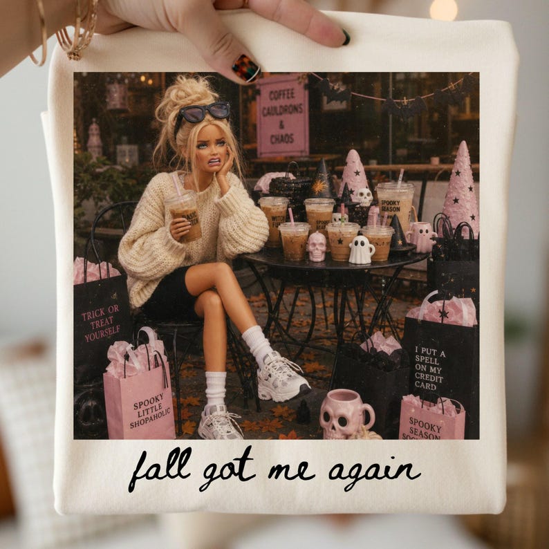 May include: A cream-colored tote bag featuring a graphic of a doll in a beige sweater and black shorts sitting at a table with coffee cups and Halloween decor. The text reads "COFFEE CAULDRONS & CHAOS", "TRICK OR TREAT YOURSELF", "I PUT A SPELL ON MY CREDIT CARD", and "fall got me again".
