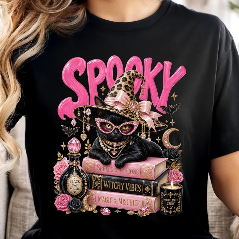 May include: A black t-shirt featuring a graphic of a black cat wearing a leopard print witch hat and pink glasses, resting on three books labeled Spells & Potions, Witchy Vibes, and Magic & Mischief, with the word SPOOKY in pink letters above.