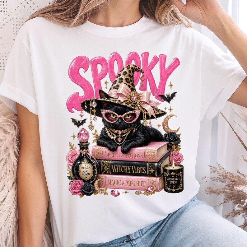 May include: A white t-shirt featuring a graphic of a black cat wearing a leopard print witch hat, pink glasses, and jewelry. The cat rests on three books labeled Spells & Potions, Witchy Vibes, and Magic & Mischief, with pink roses and text.