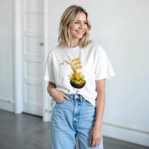 Pode incluir: Camiseta branca com um gráfico de uma tortilla mergulhando em guacamole, com o texto "Buy the Dip". O gráfico inclui um gráfico de ações. A camiseta é usada por uma pessoa.