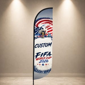 Może przedstawiać: Niestandardowa flaga piórkowa z piłką nożną, trofeum i napisem "CUSTOM FIFA WORLD CUP 2026". Projekt zawiera amerykańską flagę w kolorach czerwonym, białym i niebieskim. Flaga jest wyświetlana w pomieszczeniach.