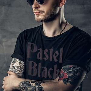 May include: Black t-shirt with the text "Pastel Black" in a dark purple font. The person is wearing sunglasses and has tattoos on their arms. The sleeves are rolled up.