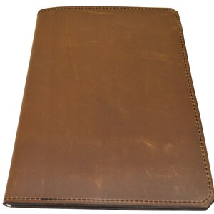 May include: A brown leather journal or notebook with a stitched border. The cover has a distressed appearance, with variations in color and texture. The notebook is rectangular and appears to be closed.