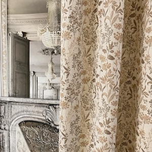 May include: Cream-colored curtain with a repeating pattern of brown and tan floral and leaf designs. The curtain is made of a textured fabric and hangs in front of a room with a fireplace and chandelier.