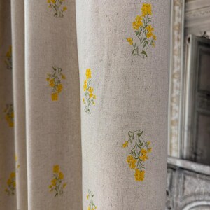 May include: Linen curtains in a natural beige hue, adorned with a repeating pattern of yellow floral motifs. The curtains are draped, showing soft folds. The floral design is simple, adding a touch of nature to the room.