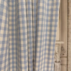 May include: Light blue and white checkered curtain panel. The fabric is folded in vertical pleats, creating a textured appearance. The pattern is a classic gingham design, suitable for home decor.