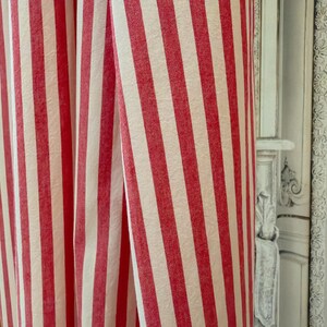 May include: Close-up of red and white striped fabric, possibly a curtain or drape. The vertical stripes create a classic pattern. The fabric appears to be of medium weight, suitable for home decor. The colour scheme is a bold, traditional design.