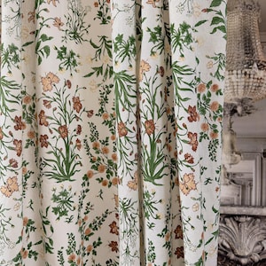 May include: Cream-colored floral curtains with a repeating pattern of orange and brown flowers, green leaves, and delicate white blossoms. The fabric is slightly textured, creating a soft, inviting look. The curtains add a touch of nature-inspired elegance to any room.