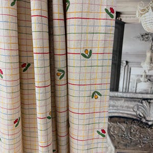 Könnte beinhalten: Cremefarbener Stoff mit einem Gittermuster aus bunten Linien und kleinen floralen Designs. Der Stoff hat rote, gelbe, grüne und blaue Linien, die das Gitter bilden. Kleine tulpenartige Blumen sind über den Stoff verstreut.