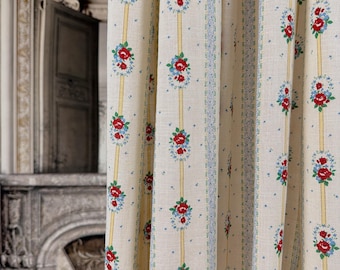 May include: Cream-colored floral curtains with a repeating pattern of red roses and blue accents. The design includes vertical yellow stripes and a blue border. The curtains are made of a textured fabric and are hanging in front of a doorway.