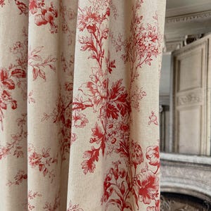 May include: Cream-coloured curtains with a repeating red floral pattern. The design features detailed illustrations of flowers and foliage, creating a classic, elegant look. The curtains are made of a textured fabric, adding depth to the design.