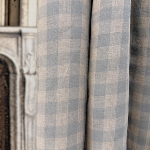 May include: Close-up of a fabric with a blue and beige checked pattern. The fabric is folded, showing the texture and weave of the material. The pattern is a classic gingham design, suitable for home decor or clothing.