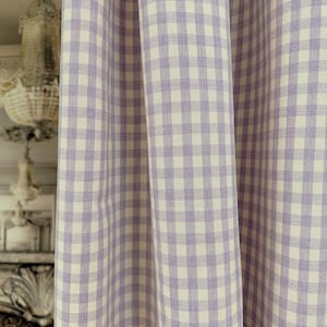 May include: Close-up of a fabric with a gingham pattern. The fabric features a repeating pattern of lavender and white squares. The fabric is draped, showing folds and texture. The background is blurred, suggesting a decorative interior.