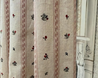 May include: Cream-colored fabric with vertical stripes in a muted red hue. The fabric is adorned with small floral patterns in red, black, and green. The design is repeated across the fabric, creating a cohesive pattern.