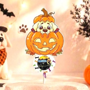 Peut inclure: Un support à sucette sur le thème d'Halloween avec une illustration de chiot clair sortant d'une citrouille orange sculptée en jack-o'-lantern. Sous la citrouille se trouve une étiquette ronde blanche avec des motifs d'os colorés.