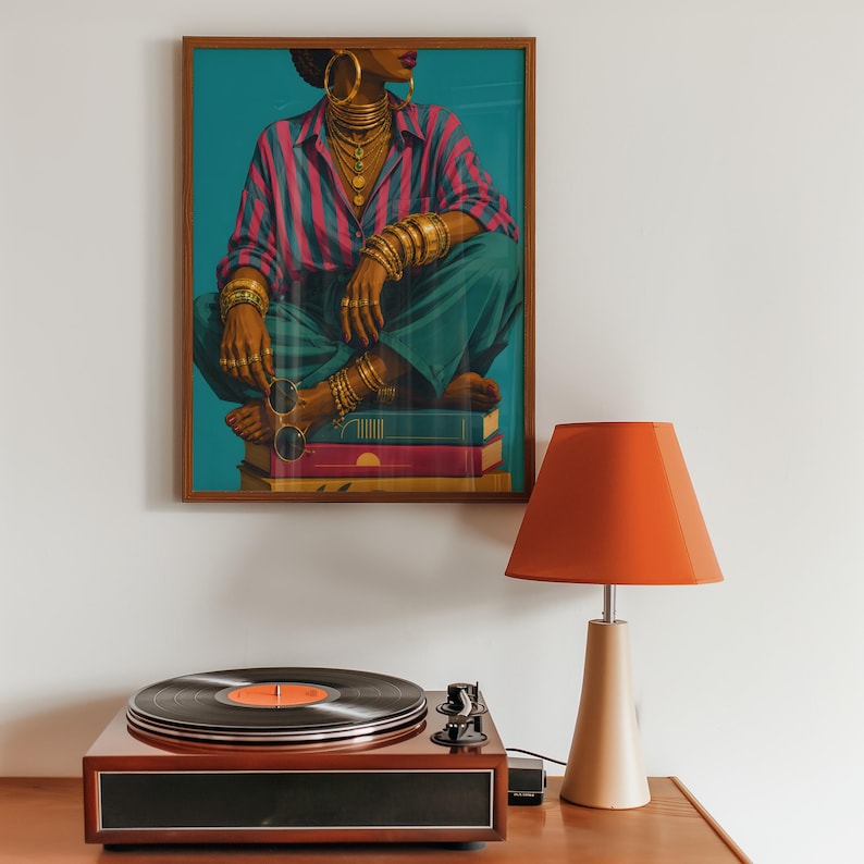 May include: A framed wall art print depicting a person wearing a pink and blue striped shirt, teal trousers, and gold jewelry, sitting on a stack of books. Below the art is a wooden record player with a black vinyl record and an orange lamp.