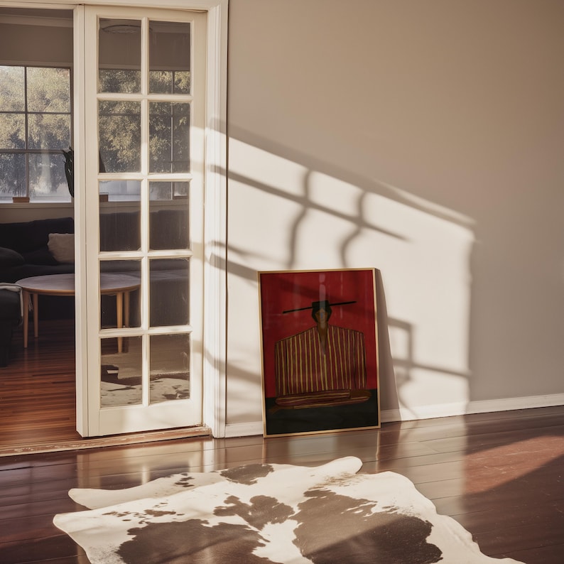 May include: A rectangular framed wall art piece featuring a stylized illustration of a figure wearing a striped garment against a deep red background, positioned on a wooden floor near a white door frame with glass panes and a cowhide rug.