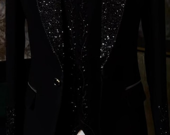 May include: Black tuxedo with a sequined lapel and bow tie. The formal suit includes a vest and a white dress shirt. The jacket has a single button closure and a pocket square. The suit is a classic formal wear ensemble.