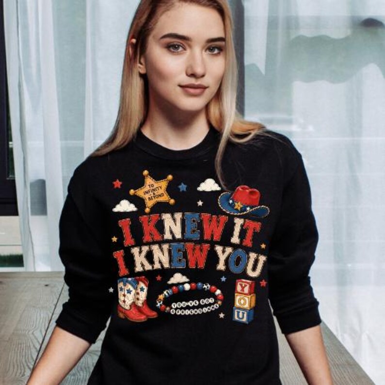 K&ouml;nnte beinhalten: Ein schwarzes Langarm-Sweatshirt mit einem Grafikdruck mit dem Text I KNEW IT I KNEW YOU, einem gelben Sheriffstern mit TO INFINITY AND BEYOND, einem Cowboyhut, rot-wei&szlig;en Stiefeln, einem Perlenarmband und gestapelten Bl&ouml;cken mit den Buchstaben Y O U.