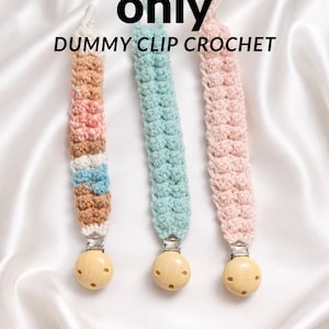 May include: Three crochet dummy clips in pastel colors. One clip is multi-colored with brown, white, pink, and blue. The other two are solid, one in light blue and the other in pink. Each clip has a wooden bead and a metal clip. Text on the image reads "Pattern only DUMMY CLIP CROCHET."