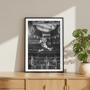 Könnte beinhalten: Schwarz-Weiß-Druck in einem Rahmen, der einen Basketballspieler in der Luft zeigt, kurz vor dem Dunk. Der Spieler trägt ein Trikot mit der Nummer 23. Der Hintergrund zeigt ein volles Stadion und den Text "NBATickets.com".