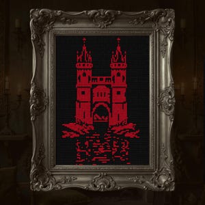 May include: A framed cross-stitch featuring a red castle design against a black background. The castle has two towers and an arched entrance. The frame is ornate with a silver finish, adding a vintage aesthetic.