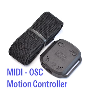 Può includere: Un controller di movimento MIDI-OSC nero con un cinturino nero abbinato. Il controller ha il testo "PIP MOTION" e diversi simboli. Il cinturino è realizzato in un materiale strutturato ed è lungo circa 30 cm.