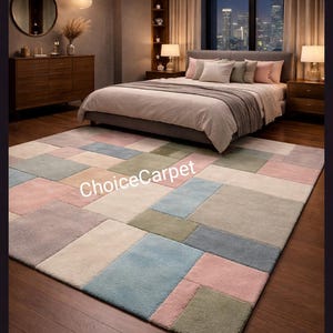 May include: A rectangular area rug with a patchwork design in shades of pink, blue, green, and beige. The rug is placed in a bedroom setting, with a bed, nightstands, and a window overlooking a cityscape. The text "ChoiceCarpet" is visible on the rug.