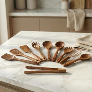Könnte beinhalten: Eine Sammlung von Küchenutensilien aus Holz, darunter Spatel, Schöpflöffel, ein Schneebesen und eine Zange, angeordnet auf einer Marmoroberfläche. Die Utensilien sind aus warm getöntem Holz gefertigt und schaffen eine natürliche Ästhetik.